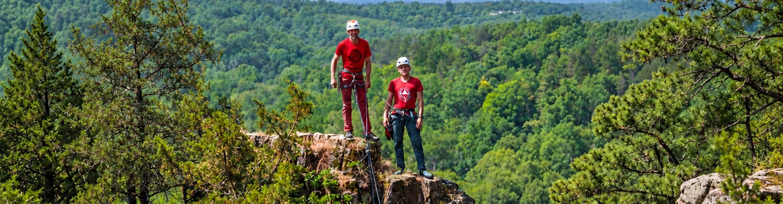 Two climbers in red shirts standing on top of the rock above the wooded Big River valley at Robinson Bluff